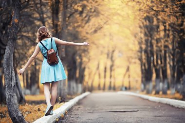 Genç kız sonbahar parkında yürüyüş yapıyor.