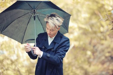 Yağmurlu havada sonbahar parkı ve şemsiyeli genç bir adam.