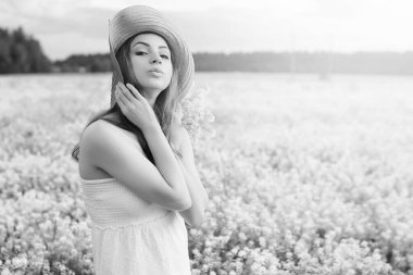 şapkalı genç kızın tek renkli resmi büyük bir çiçek tarlasında duruyor.