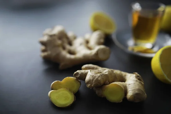 Ginger root whole and sliced. Ginger tea with lemon on the dark background. Fresh ginger root on stone background. Vitamins. Top view. Free space for your text.