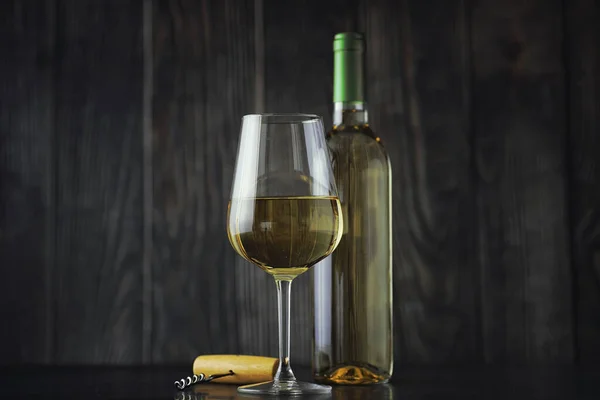 Transparent bottle of white dry wine on the table. White wine glass on a wooden wall background.
