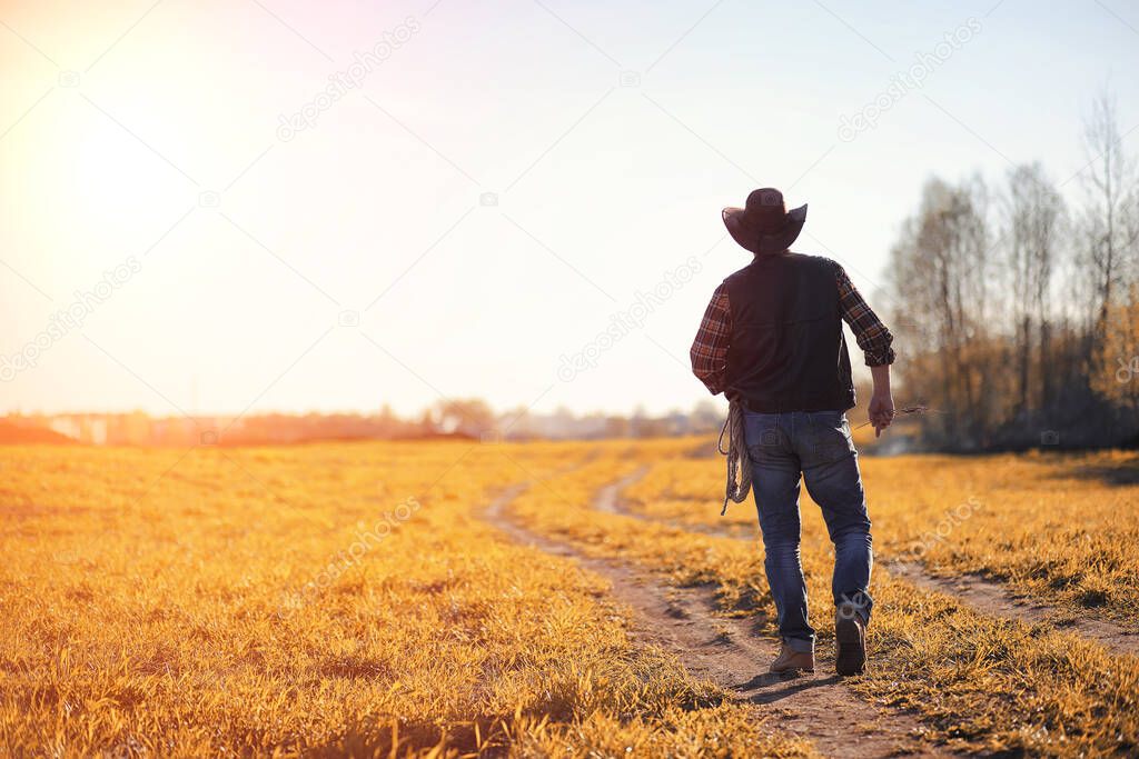 A man in a cowboy hat and a loso in the field. American farmer in a field wearing a jeans hat and with a loso. A man is walking across the field in ha