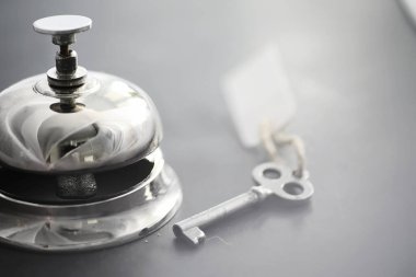Otel resepsiyonunda parlak gümüş bir metal zil. Otel odasındaki masada bir zil ve kapı anahtarıyla birlikte bir masa. Anahtar ve zil bir otelde..