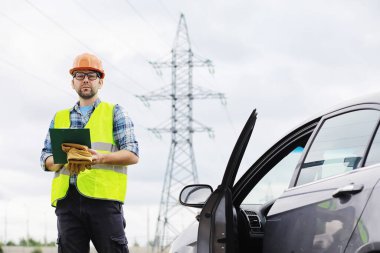 Kasklı ve üniformalı bir adam, sahada bir elektrikçi. Profesyonel elektrik mühendisi elektrik hatlarını inceliyor..