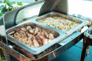 buffet chafing dish with grilled chicken slices on the left and colorful vegetable fried rice on the right, steaming hot and ready to be served at a catering event.