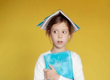 Küçük kızın kafasında kitaplar var. Ev ödevi. Sarı arkaplan