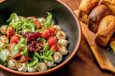 Beyaz bir masa üzerinde siyah kil kase mozzarella, kiraz domates, fesleğen ve marul ile Salata