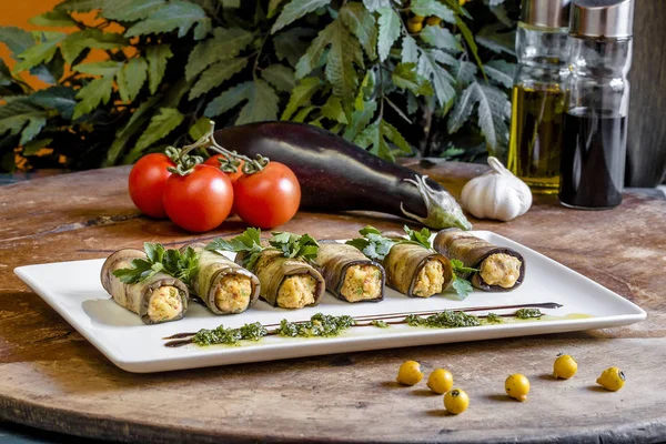 Auberginenröllchen mit Käse. georgische Küche. rustikale gebratene Auberginen mit Käse und Fleisch mit Rucola, Tomaten und Sauce auf einem Holzbrett dekoriert Stockfoto