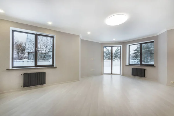 Empty living room interior with beige laminate flooring, windows and glass sliding door to the back yard