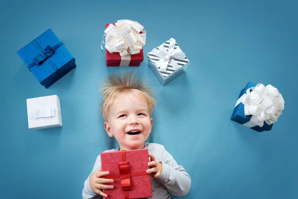 Усміхнена дитина на червоній ковдрі з подарунками — стокове фото