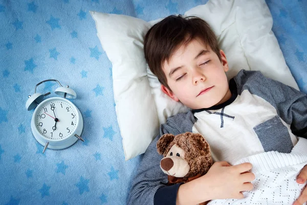 Anak enam tahun tidur di tempat tidur dengan jam alarm — Stok Foto