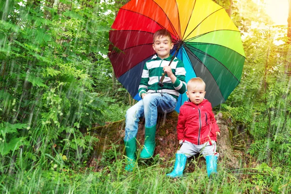 Παιδιά που κάθονται στο πάρκο με πολύχρωμη ομπρέλα — Φωτογραφία Αρχείου