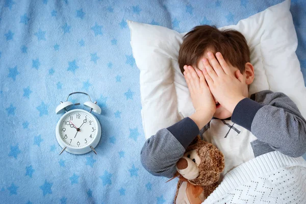 Bambino di sei anni che dorme a letto con sveglia Fotografia Stock