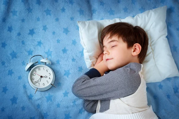 Bambino di sei anni che dorme a letto con sveglia Immagine Stock