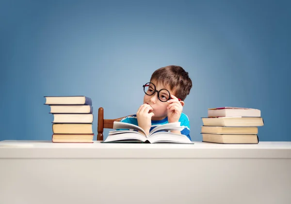 歳の子が家で本を読みます 青色の背景のテーブルに少年の勉強 — ストック写真