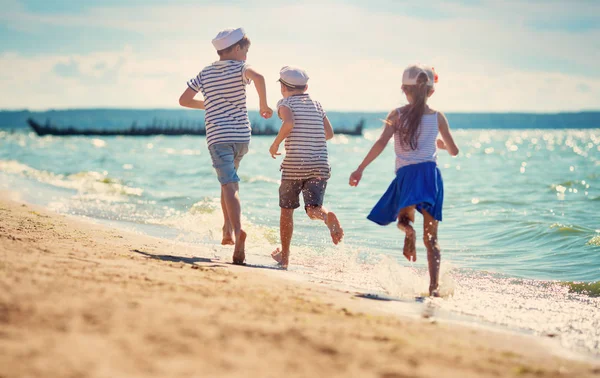 子供の夏用帽子のビーチでジャンプします 男の子と女の子が海辺で楽しい時を過す — ストック写真