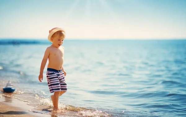 Jongen loopt op zee met strohoed op — Stockfoto