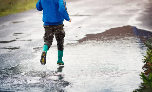 Kind läuft bei Regenwetter in Gummistiefeln in Pfütze — Stockfoto