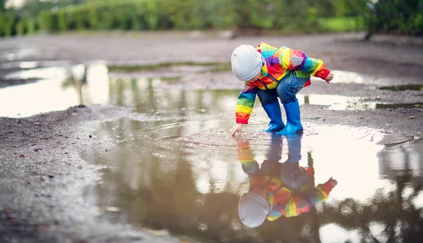 Kind läuft bei Regenwetter in Gummistiefeln in Pfütze — Stockfoto