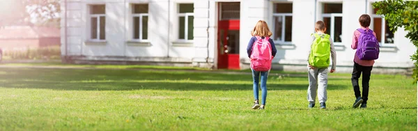 Sırt çantalı çocuklar okulun yanındaki parkta duruyorlar. — Stok fotoğraf