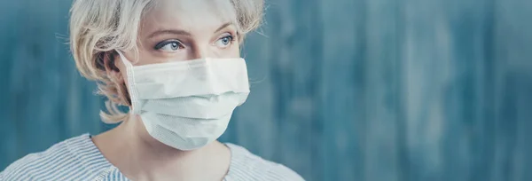 Jeune femme en masque médical de protection du visage à l'intérieur sur fond bleu — Photo