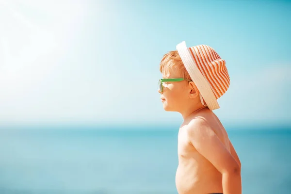 Mały chłopiec uśmiecha się na plaży w kapeluszu w okularach przeciwsłonecznych — Zdjęcie stockowe