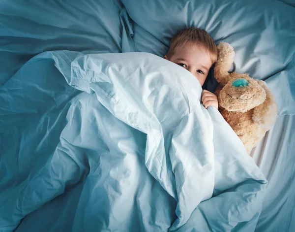 Niño somnoliento acostado en la cama con ropa de cama blanca —  Fotos de Stock