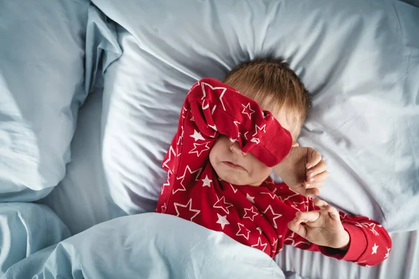 Śpiący chłopiec leżący w łóżku z niebieskimi pościelami — Zdjęcie stockowe