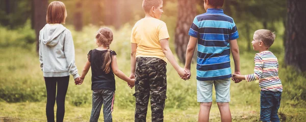 Pojkar och flickor som står i skogen och håller varandra i handen på sommarlovet — Stockfoto