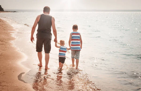 Far och söner promenader vid stranden till havs — Stockfoto