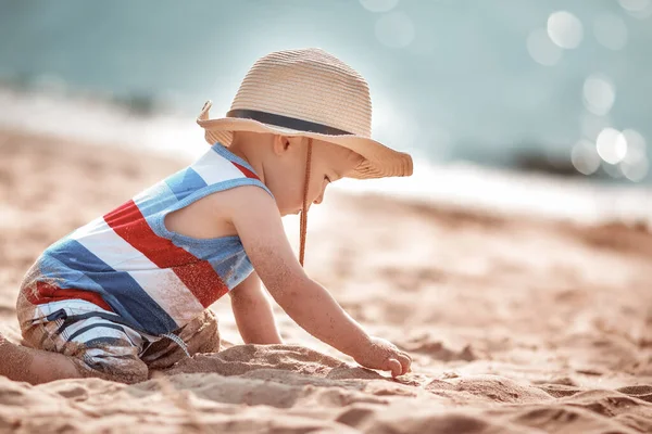 Mały chłopiec bawiący się na plaży w słomkowym kapeluszu — Zdjęcie stockowe