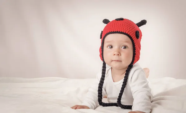 Cute baby lying in the bed on white blanket in ladybug hat — Stock Photo, Image