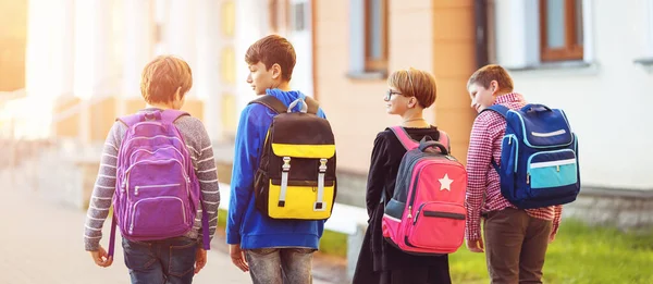 Niños con mochilas de pie en el parque cerca de la escuela — Foto de Stock