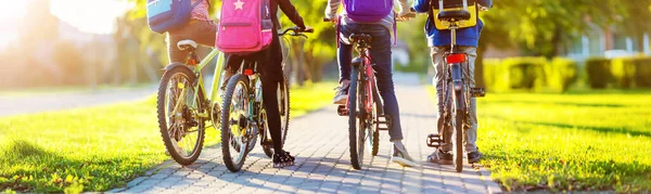 Niños con mochilas en bicicleta en el parque cerca de la escuela —  Fotos de Stock