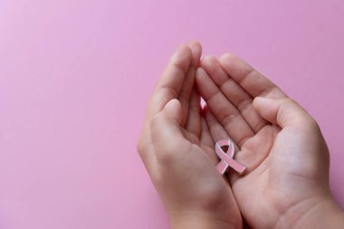 Küçük pembe farkındalık kurdelesini tutan bir el. Uzayı metin için kopyala. Göğüs kanseri farkındalığı konsepti.