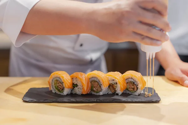 手シェフが 日本の寿司 サーモンのロールにソースを注いで — ストック写真