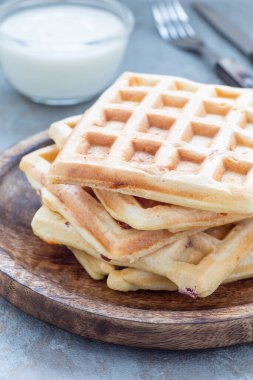 Ev yapımı lezzetli Belçika waffleları, domuz pastırması ve dilimlenmiş peynirle, sade yoğurtla servis edilmiş, tahta tabakta, dikey.