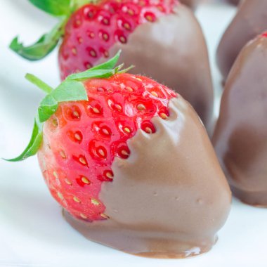 Beyaz bir tabakta sütlü çikolatayla kaplı çilekler, yakın plan, kare format