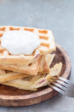 Domuz pastırması ve dilimlenmiş peynirli ev yapımı Belçika waffleları, tahta bir tabakta sade yoğurt ile servis ediliyor, dikey, kopyalama alanı.