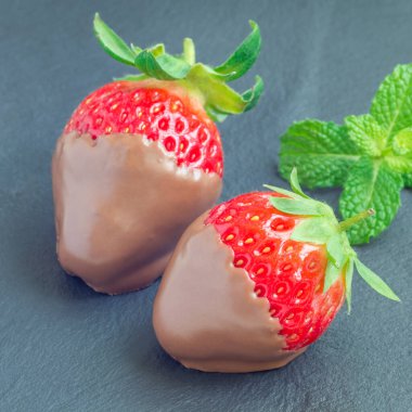 Gri bir levhada sütlü çikolatayla kaplı çilekler, taş, yakın plan, kare format