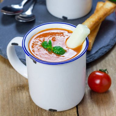 Bardakta ev yapımı fesleğen çorbası, mozzarella peyniri çubuğu ve kızarmış ekmekle servis ediliyor, kare formatta.