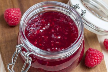 Ahşap bir tahtanın üzerinde cam kavanozda ahududu reçeli.