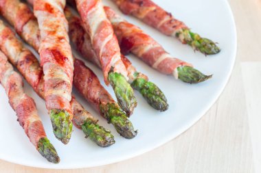 Beyaz bir tabağa sarılı yeşil kuşkonmaz, yatay.