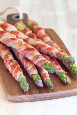 Sağlıklı aperatif, ahşap tahtaya sarılı yeşil kuşkonmaz, dikey.