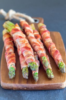 Sağlıklı aperatif, ahşap tahtaya sarılı yeşil kuşkonmaz, dikey.