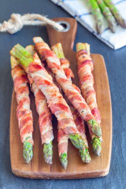 Sağlıklı aperatif, ahşap tahtaya sarılı yeşil kuşkonmaz, dikey.