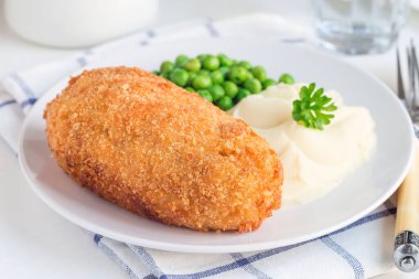 Tavuk Kiev, Ukrayna mutfağı. Tereyağı ve otla doldurulmuş ekmek kırıntıları içinde tavuk pirzolası, patates püresi ve yeşil bezelyeyle servis edilmiş, beyaz bir tabakta, yatay olarak.