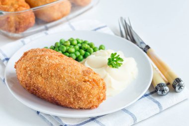 Tavuk Kiev, Ukrayna mutfağı. Tereyağı ve otla doldurulmuş ekmek kırıntıları içinde tavuk pirzolası, patates püresi ve yeşil bezelyeyle servis edilmiş, beyaz bir tabakta, yatay olarak.