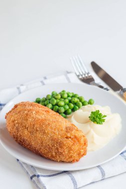 Tavuk Kiev, Ukrayna mutfağı. Tereyağı ve otla doldurulmuş ekmek kırıntıları içinde tavuk pirzolası, patates püresi ve yeşil bezelye ile servis edilmiş, beyaz arka planda, dikey, kopyalama alanı