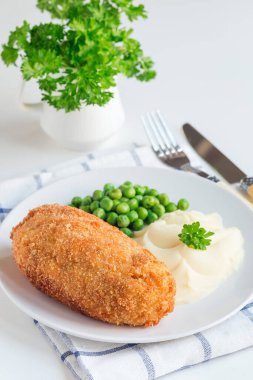 Tavuk Kiev, Ukrayna mutfağı. Tereyağı ve otla doldurulmuş ekmek kırıntıları içinde tavuk pirzolası, patates püresi ve yeşil bezelye ile servis edilmiş, beyaz bir tabakta, dikey